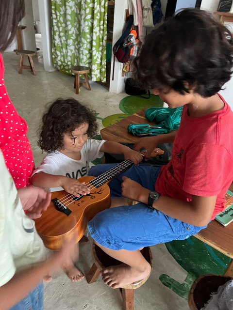 Un niño mayor le muestra el ukulele a uno pequeño